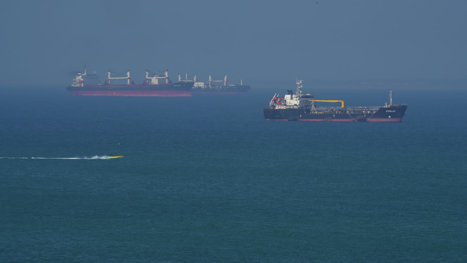 Oil tankers and a cargo ship sit at anchor on calm blue water near the Strait of Hormuz under a hazy sky, illustrating the June 15 2026 ThriveInMarkets morning analysis as a US-Iran peace deal set to reopen the strait sent WTI crude tumbling about 5 percent to 80.49 dollars, while Bitcoin rose to 65,627 dollars, Ethereum to 1,716 dollars, gold firmed to 4,219 dollars and the S&P 500 held near its 7,431 record ahead of Kevin Warsh's first FOMC meeting and dot plot on Wednesday June 17