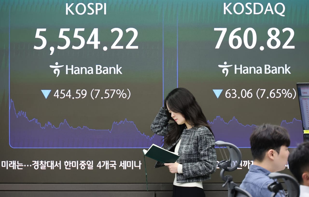 A dealer walks past a Hana Bank board in Seoul showing the Kospi at 5,554.22 down 7.57 percent, used as the ThriveInMarkets weekend recap hero for October 12 to October 18 2026, when the Nasdaq Composite closed Friday at 26,140.03 down 4.5 percent on the week, its worst week since June, after South Korea's Kospi triggered circuit breakers